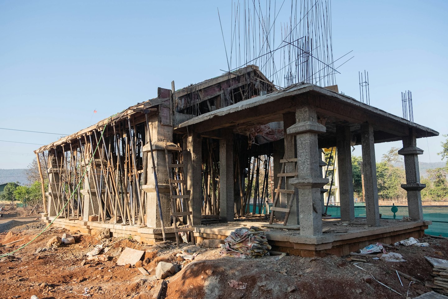 Edificio de hormigón en construcción con andamios metálicos y barras de refuerzo expuestas.