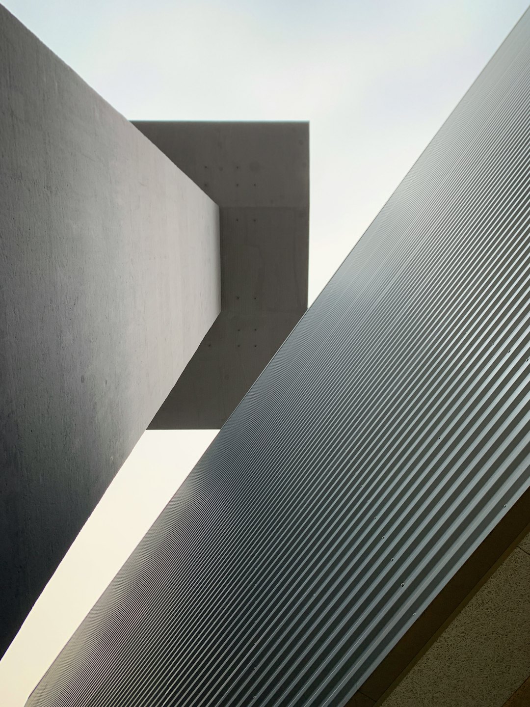 Edificio de hormigón gris con fachada de metal corrugado y ángulos agudos.