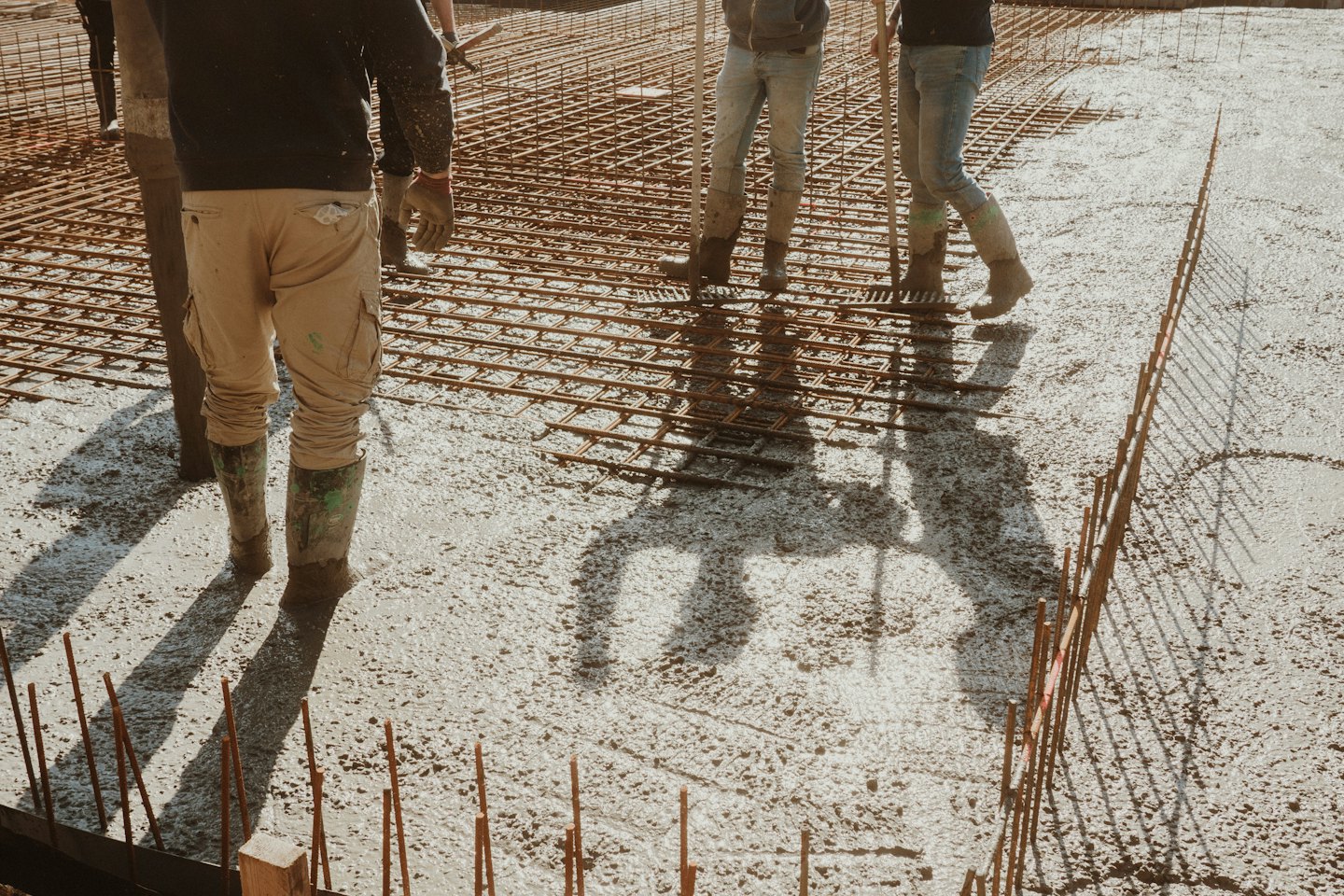 Obreros de la construcción nivelan concreto fresco sobre una rejilla de varillas de acero.