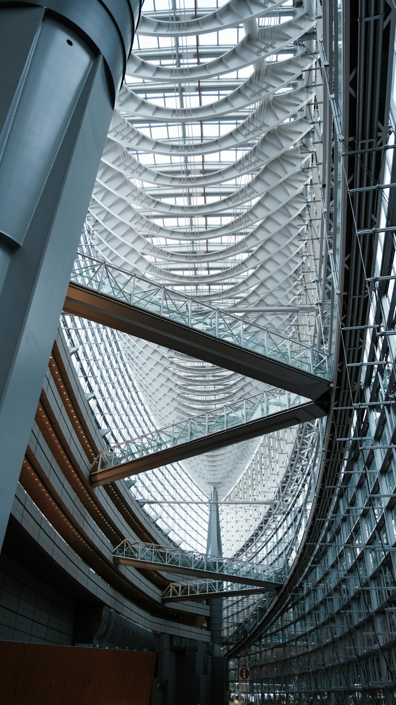 Interior de edificio moderno con pasarelas escalonadas y techo ondulado.
